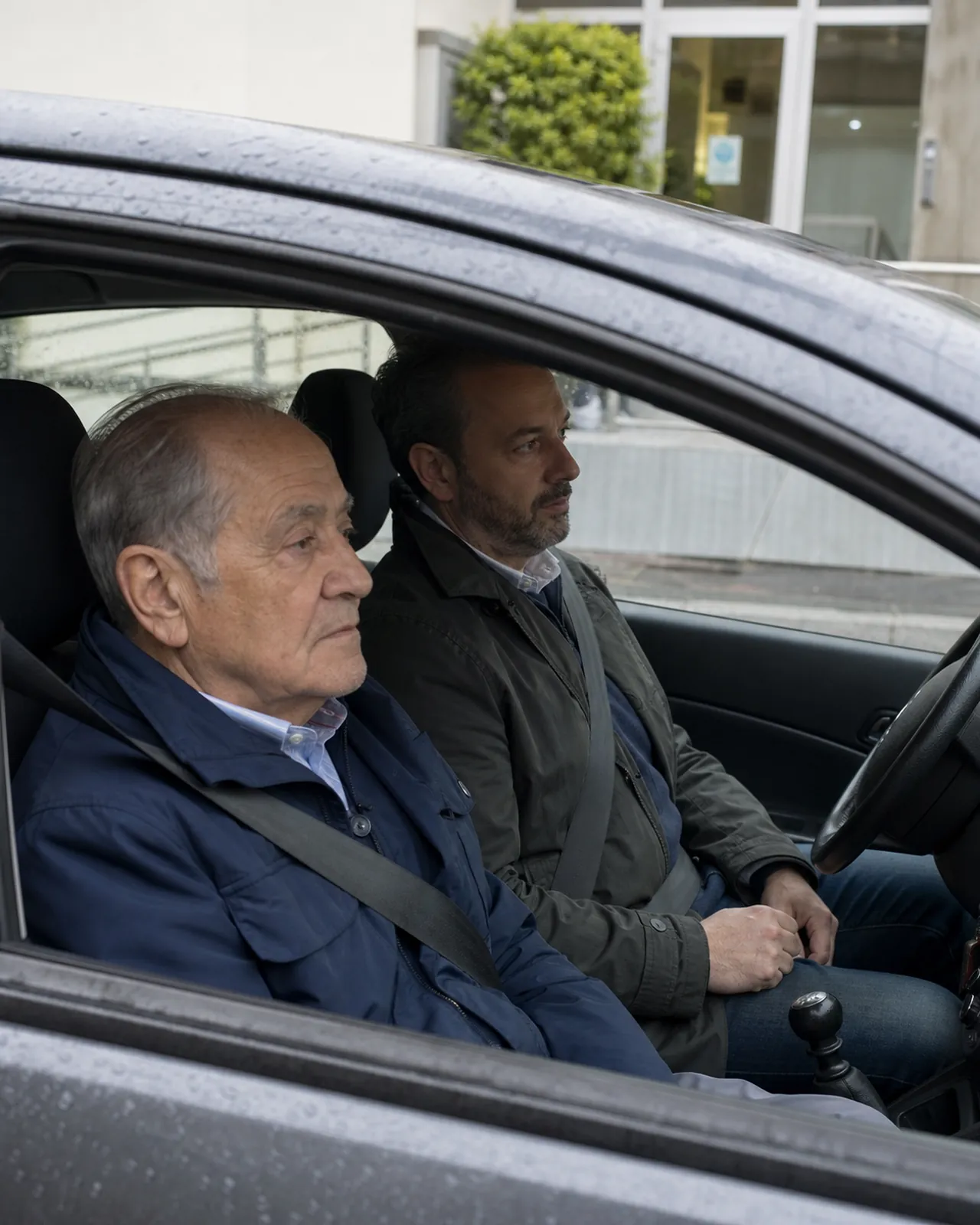 Uomo anziano e accompagnatore aspettano in un'auto parcheggiata vicino a un ambulatorio di Padova